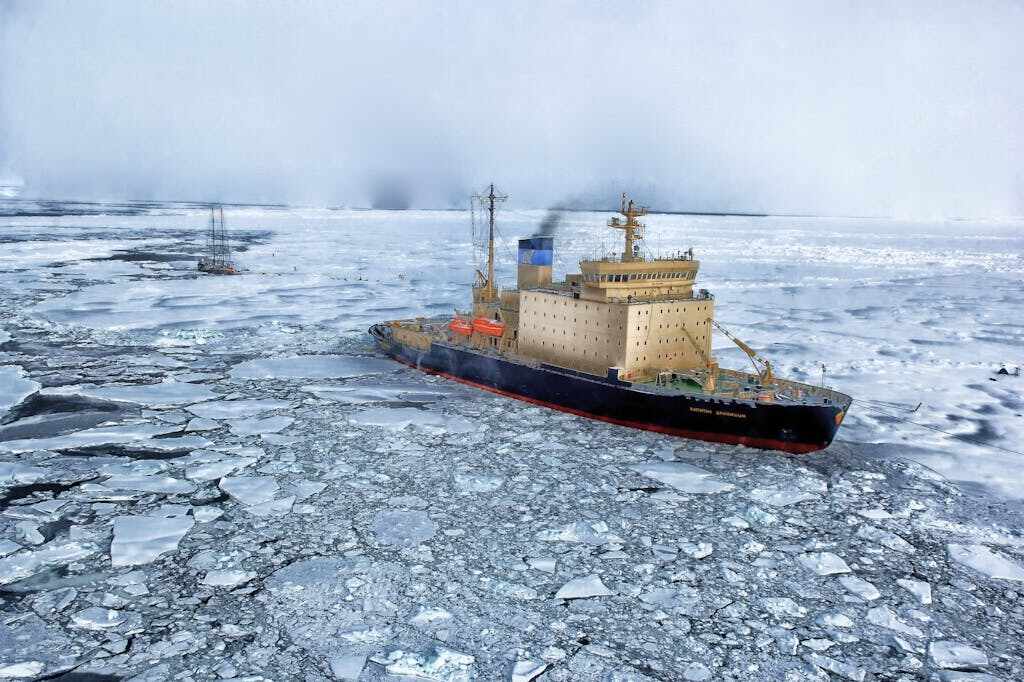Research vessel navigating through fragmented sea ice in Antarctica, with broken ice floes surrounding the ship against a misty polar backdrop.