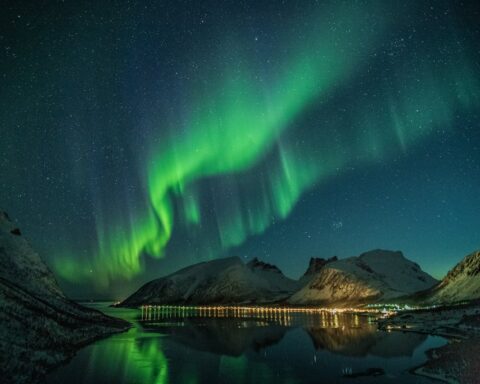 Aurora over a calm lake at night with green arcs reflecting on the water
