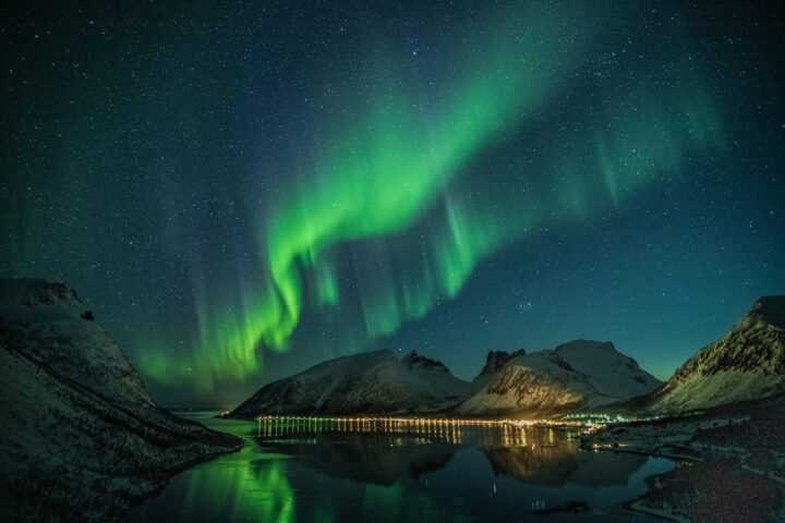 Aurora over a calm lake at night with green arcs reflecting on the water