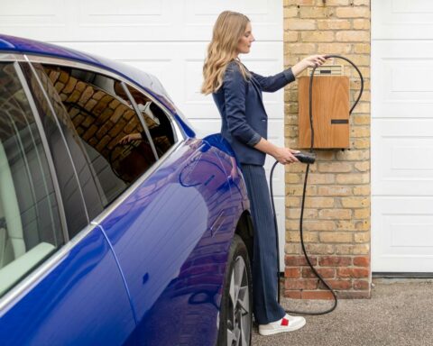 Woman in business attire charging a blue electric vehicle at a wall-mounted home charger