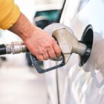 Close-up of a person's hand holding a fuel pump nozzle while refueling a white car at a gas station