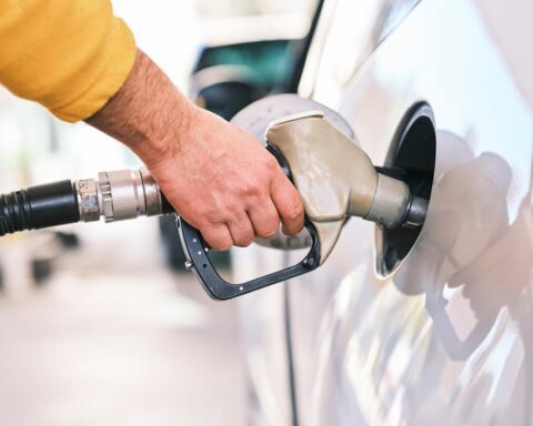 Close-up of a person's hand holding a fuel pump nozzle while refueling a white car at a gas station