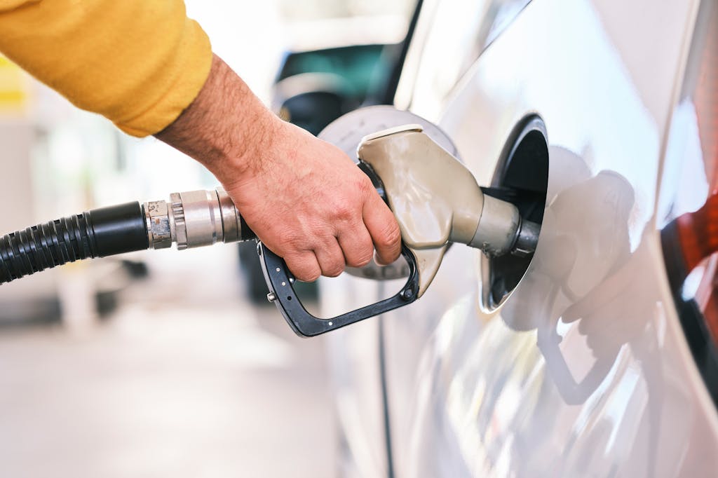 Close-up of a person's hand holding a fuel pump nozzle while refueling a white car at a gas station
