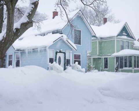 Snow-covered neighborhood street with houses during a winter storm, low clouds, and plowed road.