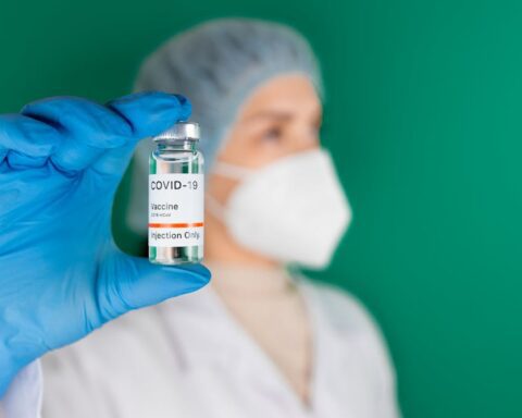 Gloved hand holding a COVID-19 vaccine vial and syringe