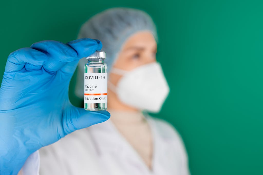 Gloved hand holding a COVID‑19 vaccine vial and syringe