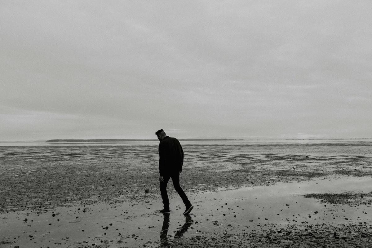 A solitary figure walking alone on a beach shoreline, silhouetted against an overcast sky, representing depression and isolation.