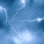 Lightning over storm clouds at night above a coastline, long exposure bolts against dark sky