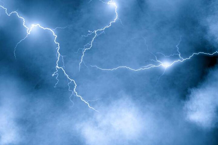 Lightning over storm clouds at night above a coastline, long exposure bolts against dark sky