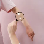 Person holding a magnifying glass over a white surface, symbolizing close examination and vigilance in detecting early skin changes.