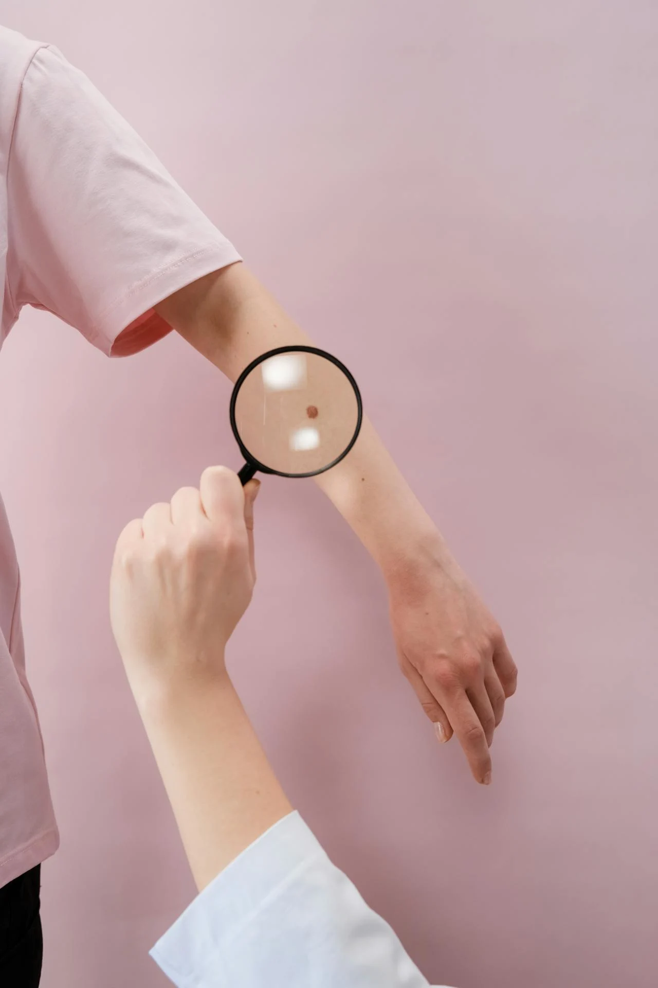 Close-up of a hand holding a magnifying glass on a white background, used as the feature image for a skin-cancer prevention explainer