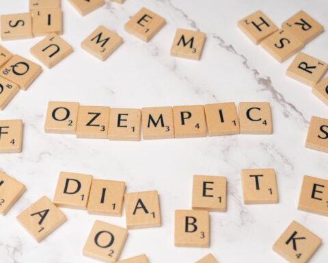 Scrabble tiles on a marble surface spelling out "OZEMPIC" with other random letters arranged around it.
