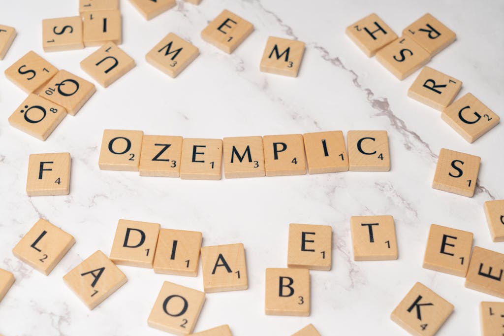 Scrabble tiles on a marble surface spelling out "OZEMPIC" with other random letters arranged around it.