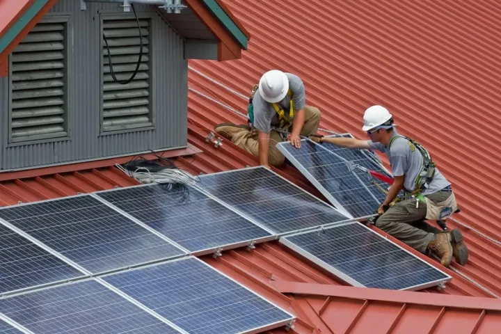 Two workers installing solar panels on a red metal roof of a building in Wayne National Forest.