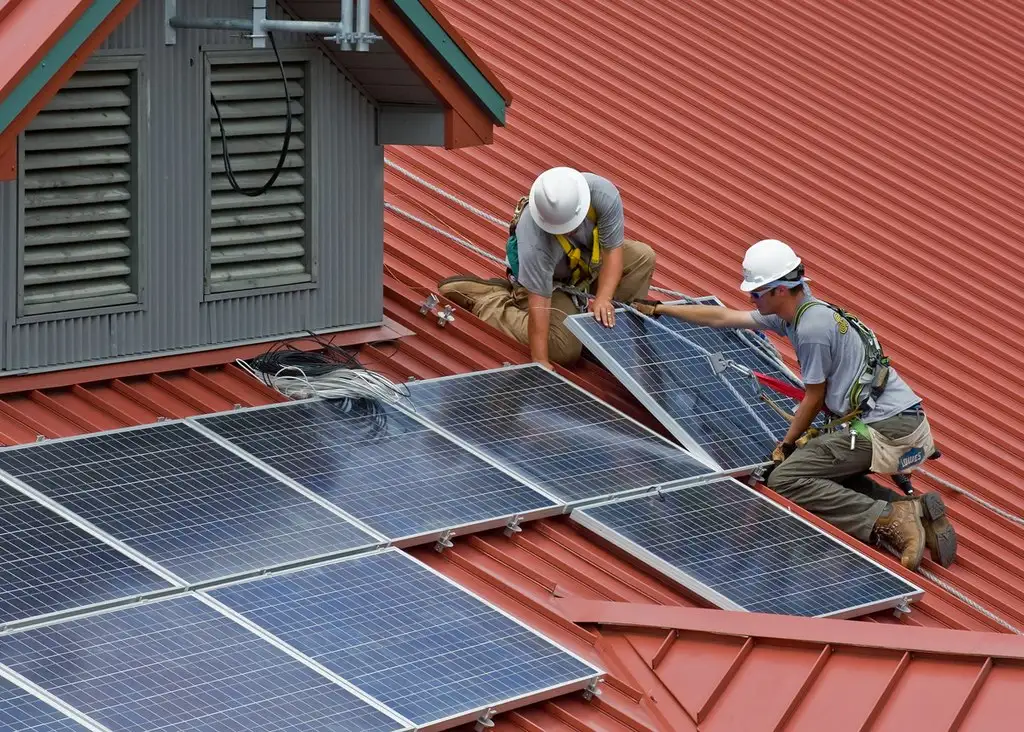 Two workers installing solar panels on a red metal roof of a building in Wayne National Forest.