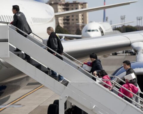 Passengers in a queue at an airport gate walking toward an aircraft jet bridge, carrying luggage and boarding.