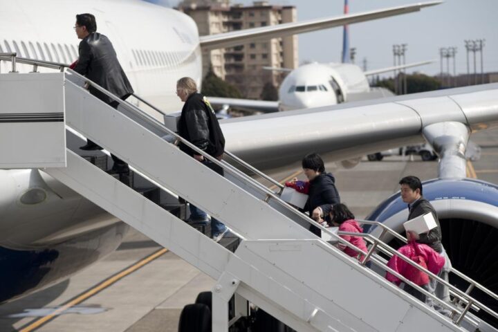 Passengers in a queue at an airport gate walking toward an aircraft jet bridge, carrying luggage and boarding.