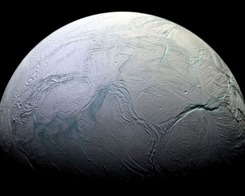 A detailed, close-up image of Enceladus, Saturn's icy moon, showing its heavily cratered and fractured surface with prominent ridges and troughs, illuminated against the darkness of space.