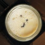 Overhead view of a jar of foamy warm milk with a few ants floating on the surface.