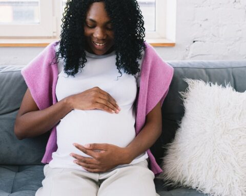 Pregnant Black woman sitting comfortably on a couch at home with a slight smile