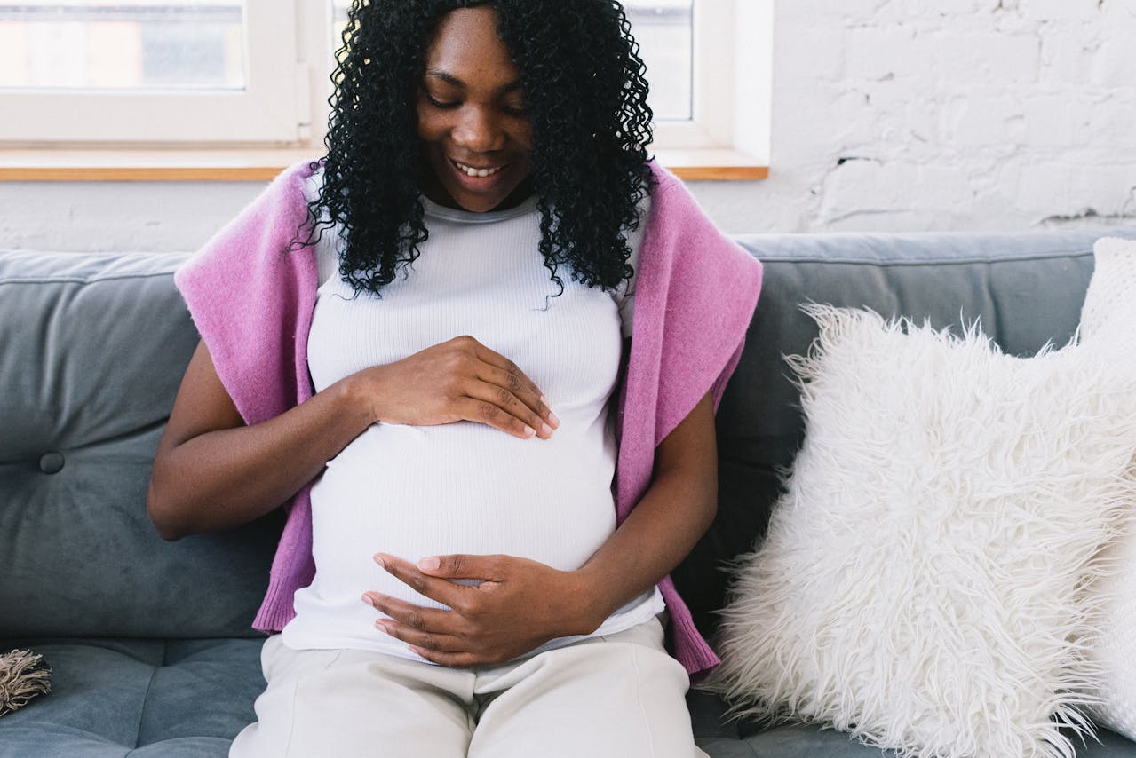 Pregnant Black woman sitting comfortably on a couch at home with a slight smile