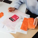 Person holding receipts and using a calculator on a desk, close-up budgeting scene