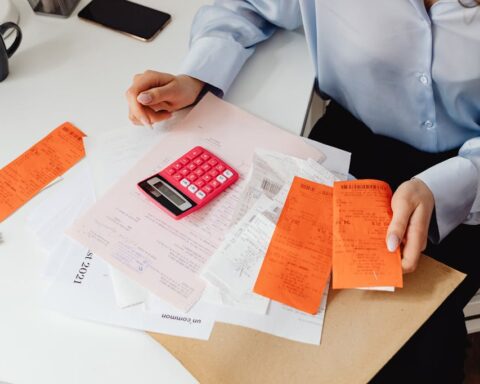 Person holding receipts and using a calculator on a desk, close-up budgeting scene