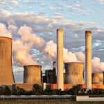 Large power plant with multiple chimneys and cooling towers releasing steam under a cloudy sky