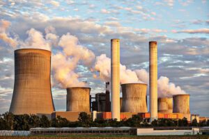 Large power plant with multiple chimneys and cooling towers releasing steam under a cloudy sky