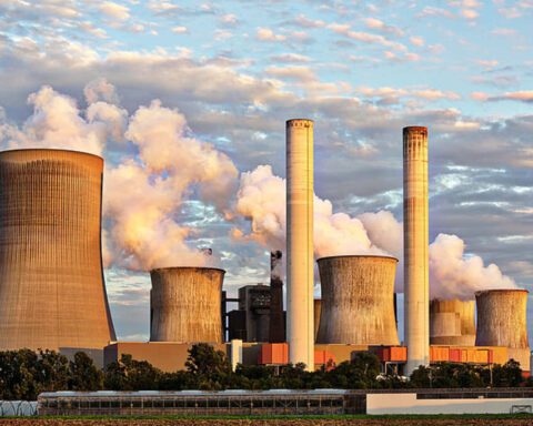 Large power plant with multiple chimneys and cooling towers releasing steam under a cloudy sky