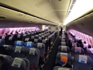 Nearly empty PEK–LAX aircraft cabin in March 2020 during COVID-19, with rows of vacant seats under purple cabin lighting.