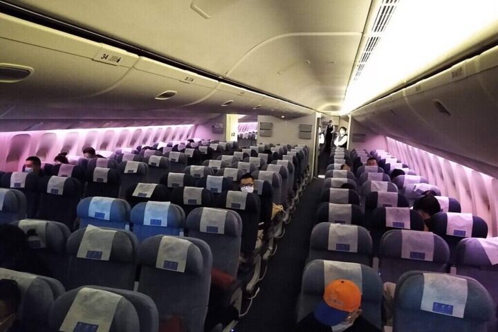 Nearly empty PEK–LAX aircraft cabin in March 2020 during COVID-19, with rows of vacant seats under purple cabin lighting.