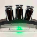 A miniature concrete arch supporting three metal weights, with a green LED light glowing underneath, demonstrating the material's dual functionality for load bearing and powering electronics.