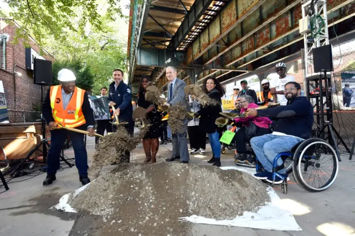 MTA officials and community members, including a person in a wheelchair, participate in the groundbreaking ceremony for the Middletown Road station accessibility project, shoveling dirt to mark the start of construction.
