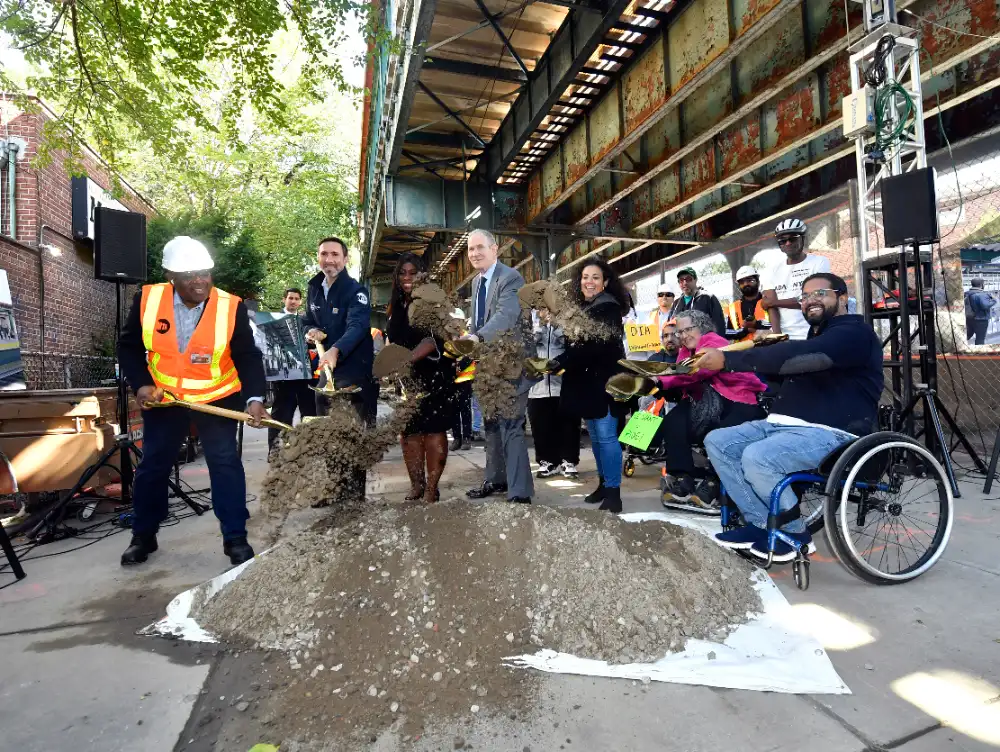 MTA officials and community members, including a person in a wheelchair, participate in the groundbreaking ceremony for the Middletown Road station accessibility project, shoveling dirt to mark the start of construction.