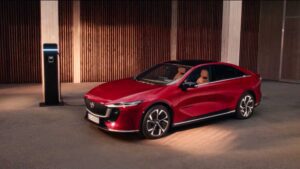 Mazda 6e electric sedan in red, three-quarter view while charging, promotional image from Mazda Australia
