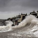 Storm surge waves violently crashing against coastal houses in Port William, Galloway, Scotland, demonstrating the destructive power of severe coastal storms.