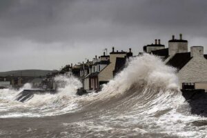 Storm surge waves violently crashing against coastal houses in Port William, Galloway, Scotland, demonstrating the destructive power of severe coastal storms.