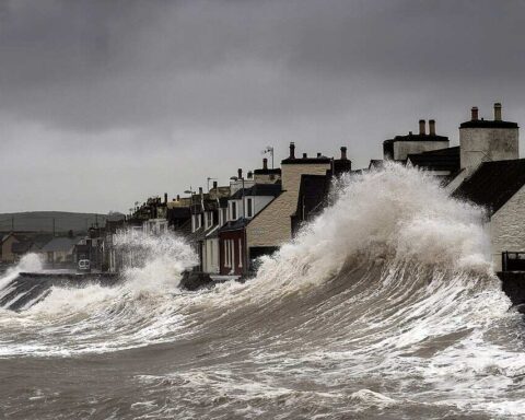 Storm surge waves violently crashing against coastal houses in Port William, Galloway, Scotland, demonstrating the destructive power of severe coastal storms.