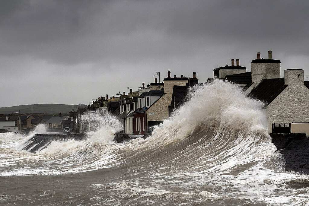Storm surge waves violently crashing against coastal houses in Port William, Galloway, Scotland, demonstrating the destructive power of severe coastal storms.