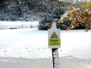 Thin ice on a UK waterbody with a cracked frozen surface in low winter light, close-up texture visible.