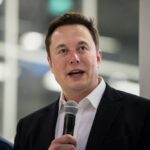 Elon Musk speaking at SpaceX HQ in front of a Crew Dragon capsule, answering media questions.