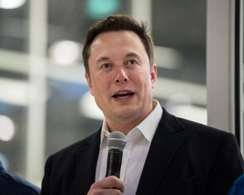 Elon Musk speaking at SpaceX HQ in front of a Crew Dragon capsule, answering media questions.