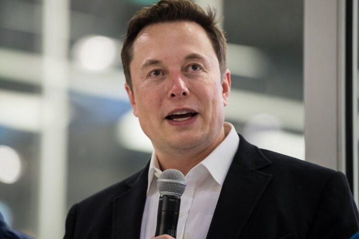 Elon Musk speaking at SpaceX HQ in front of a Crew Dragon capsule, answering media questions.
