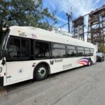 New white NJ Transit bus parked on a street with a bridge structure visible in the background