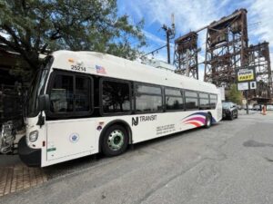 New white NJ Transit bus parked on a street with a bridge structure visible in the background