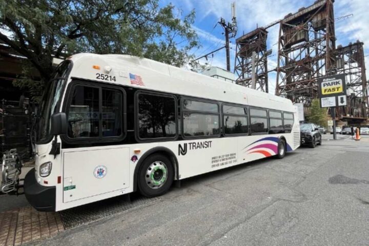 New white NJ Transit bus parked on a street with a bridge structure visible in the background