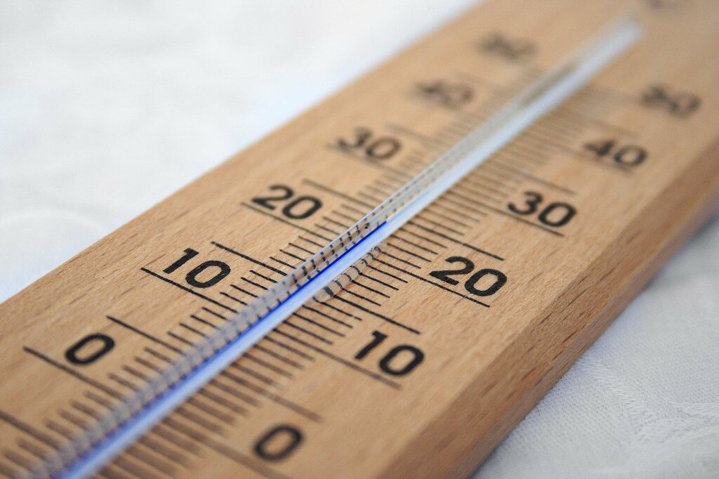 Close-up of a wooden Celsius thermometer with blue liquid column and shallow depth of field.