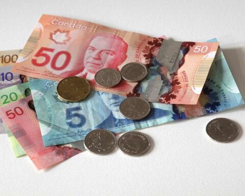 Canadian dollar bills and coins including $5, $10, $20, and $50 notes with various coins scattered on a white surface