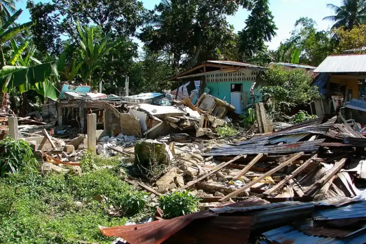 Collapsed home and debris in Loon, Bohol, Philippines after a strong quake, with nearby houses and trees in daylight